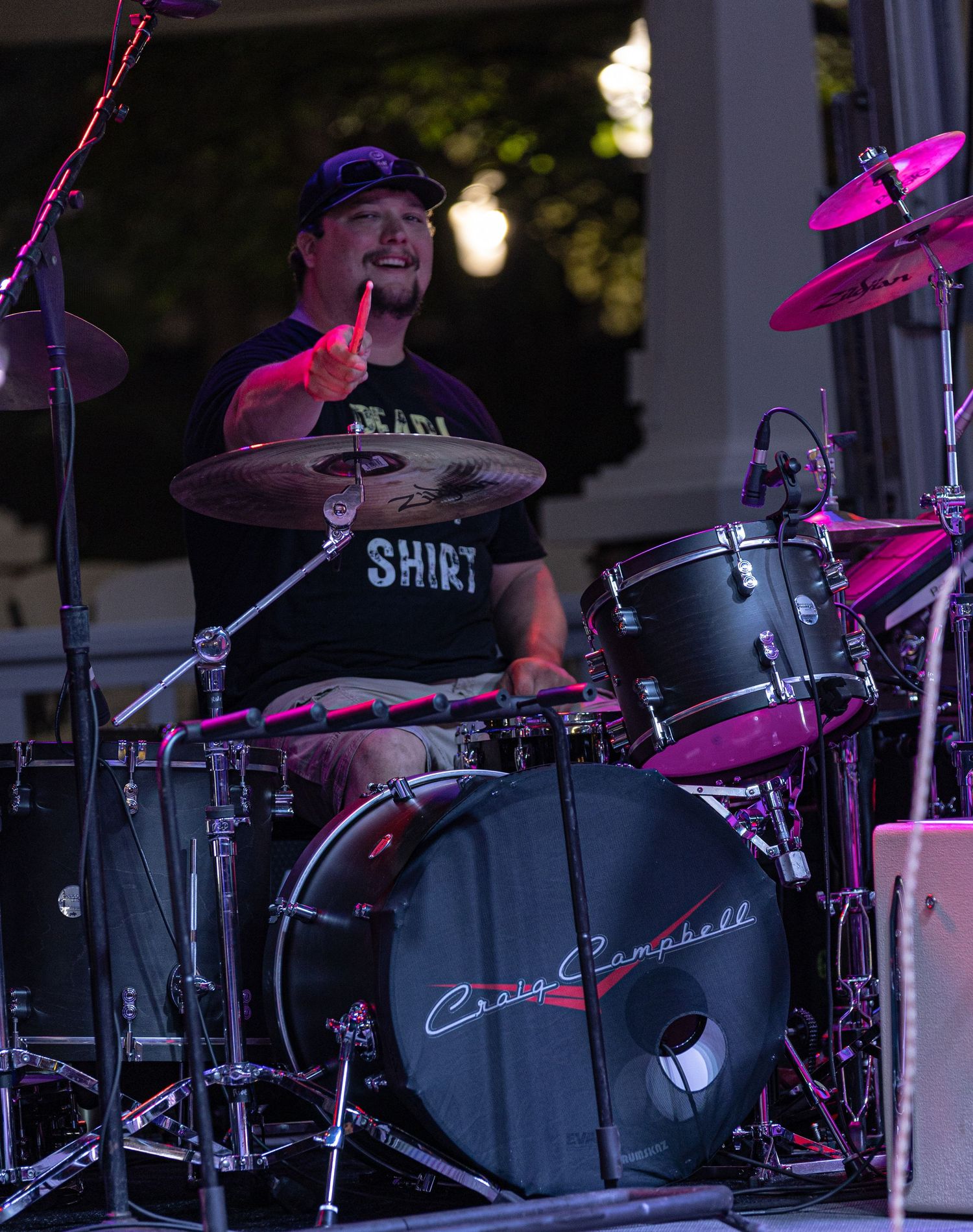 Drummer Craig Campbell performs live on stage with a full drum kit, cymbals, and band members visible in foreground.