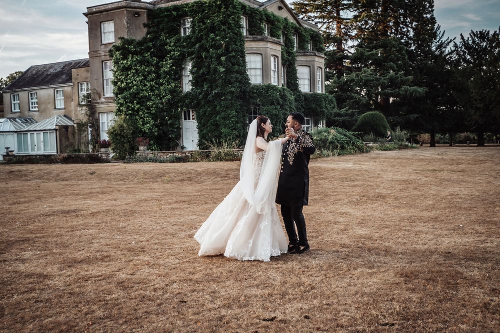 Bride and groom share a romantic moment on golden lawn before ivy-covered English manor wedding venue.