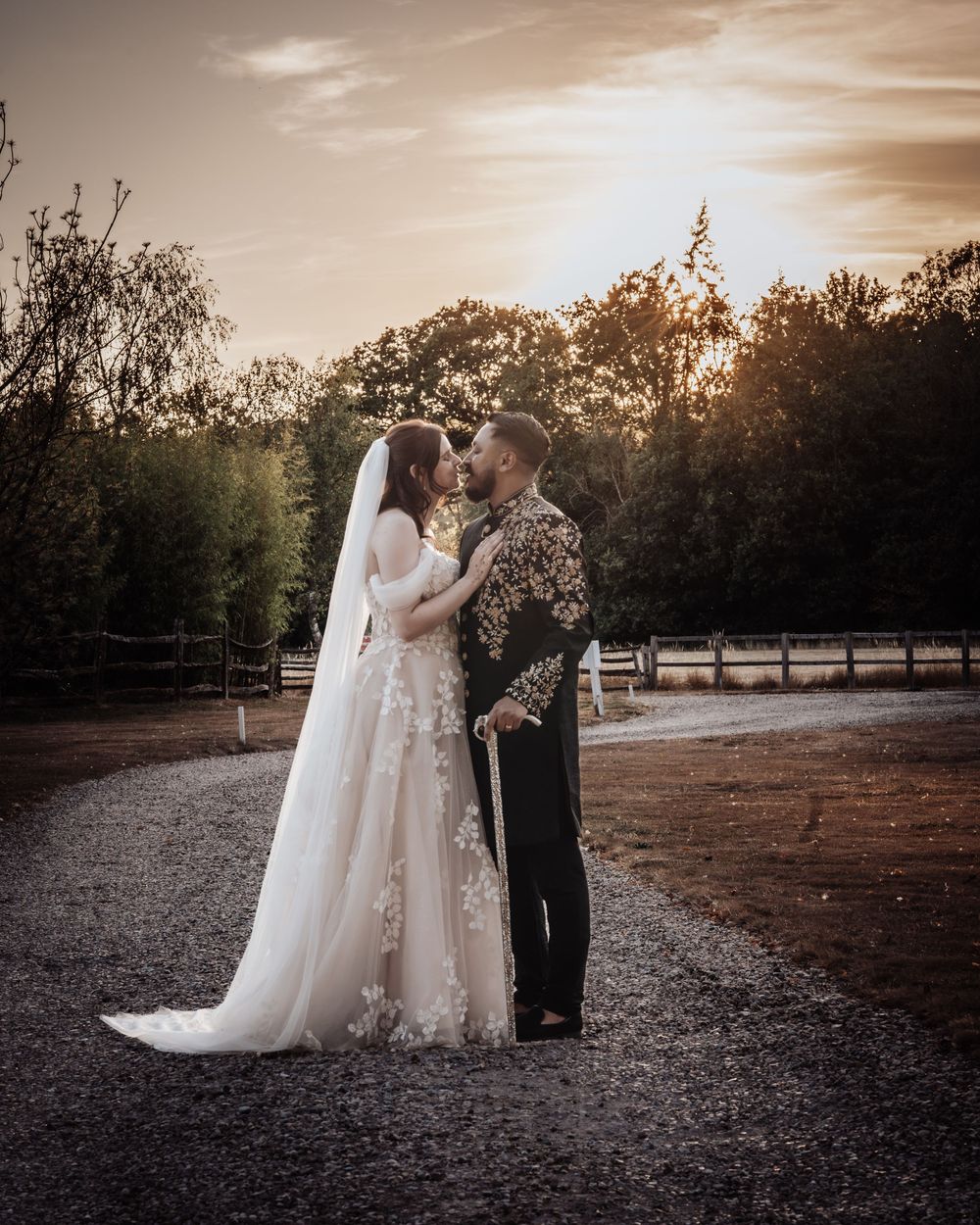 Bride and groom share a romantic sunset kiss in a scenic outdoor wedding setting with golden hour lighting.