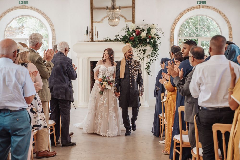 Bride and groom walk down the aisle together at an elegant indoor wedding ceremony with floral arch.