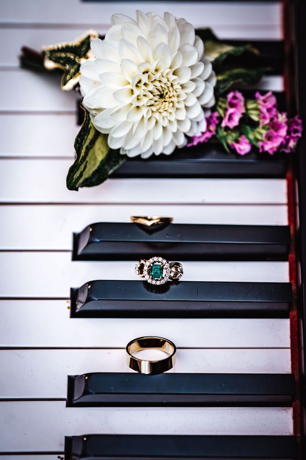 Wedding rings and white dahlia flower displayed on black and white piano keys.