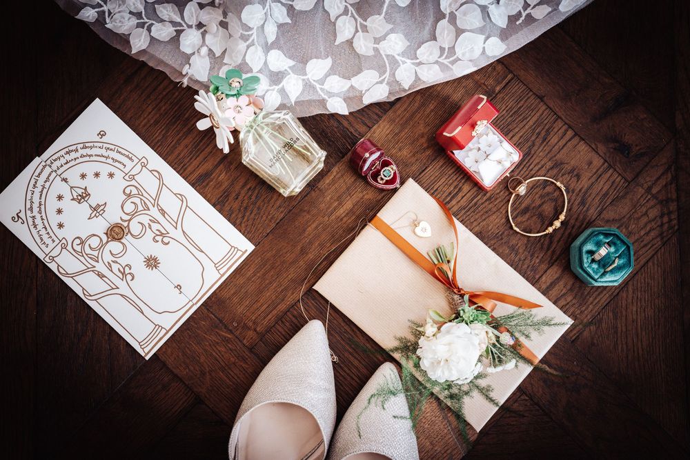 Flat lay of wedding details including shoes, bouquet, rings, and stationery on wooden floor.
