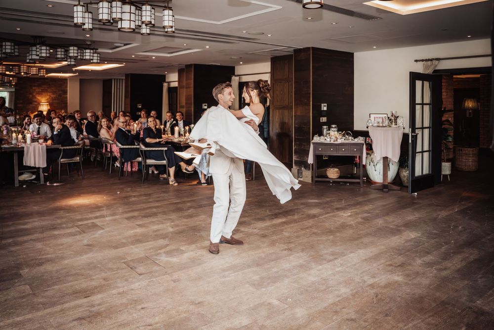 Groom lifting bride during first dance at elegant wedding reception with guests seated in background.