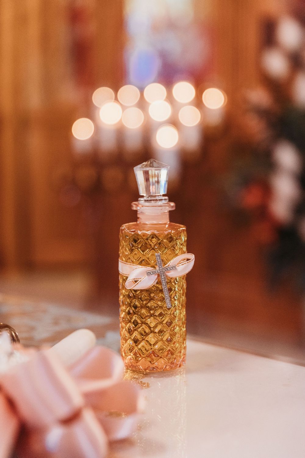 Elegant golden perfume bottle with crystal stopper and ribbon bow on white surface with bokeh candle lights background.