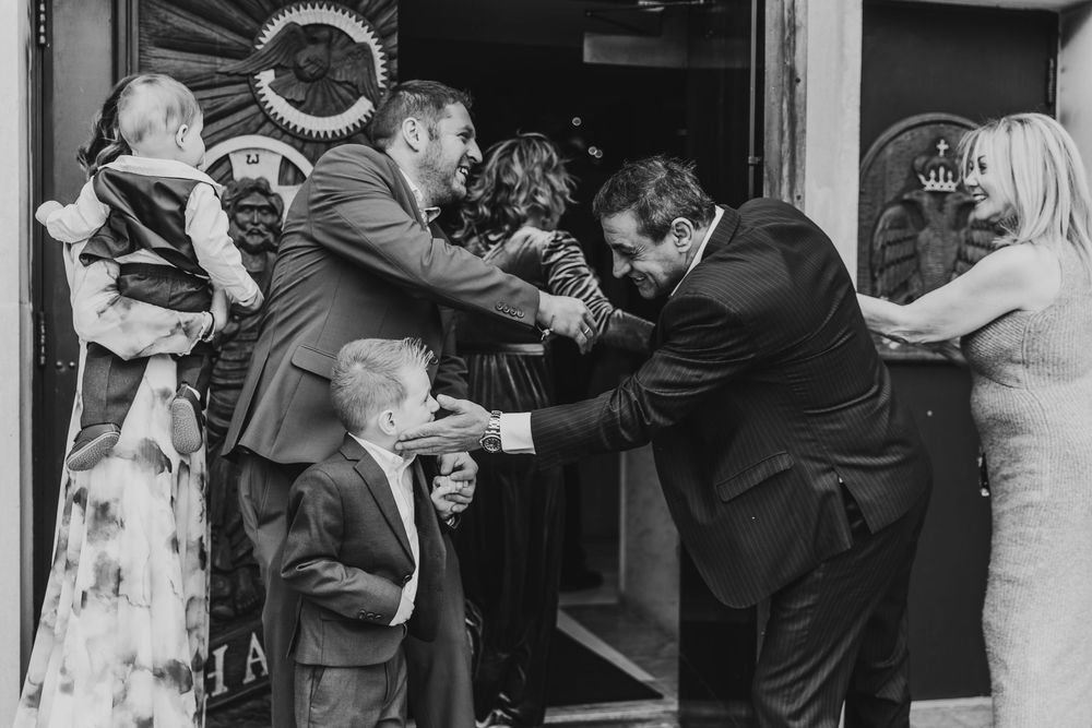 Black and white wedding photo of guests greeting each other at a doorway, including children in formal attire.
