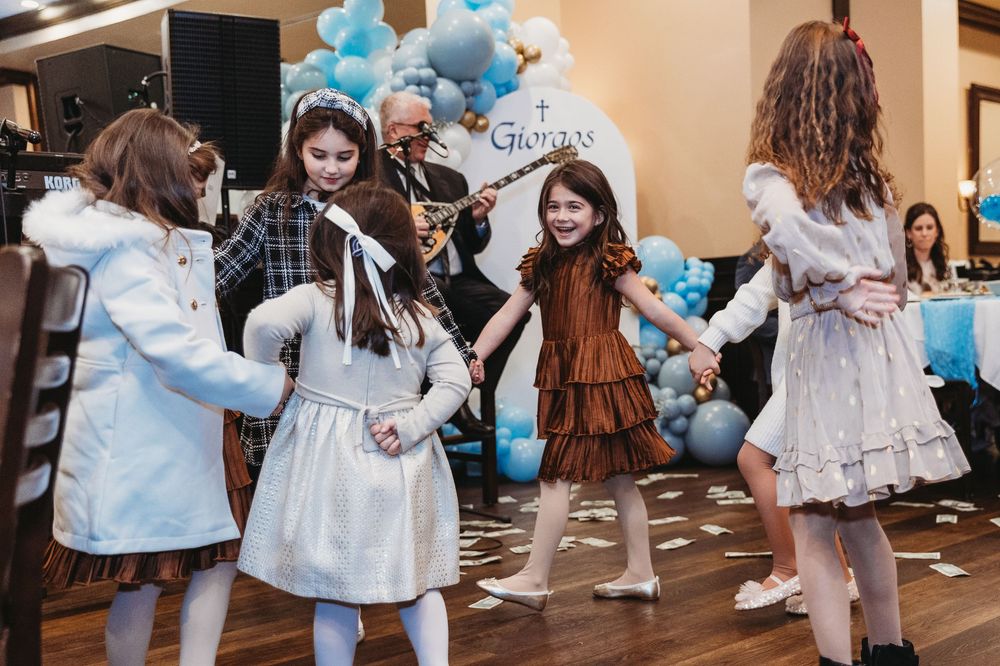 Girls in dresses dancing together at a festive blue and white balloon-decorated celebration party.