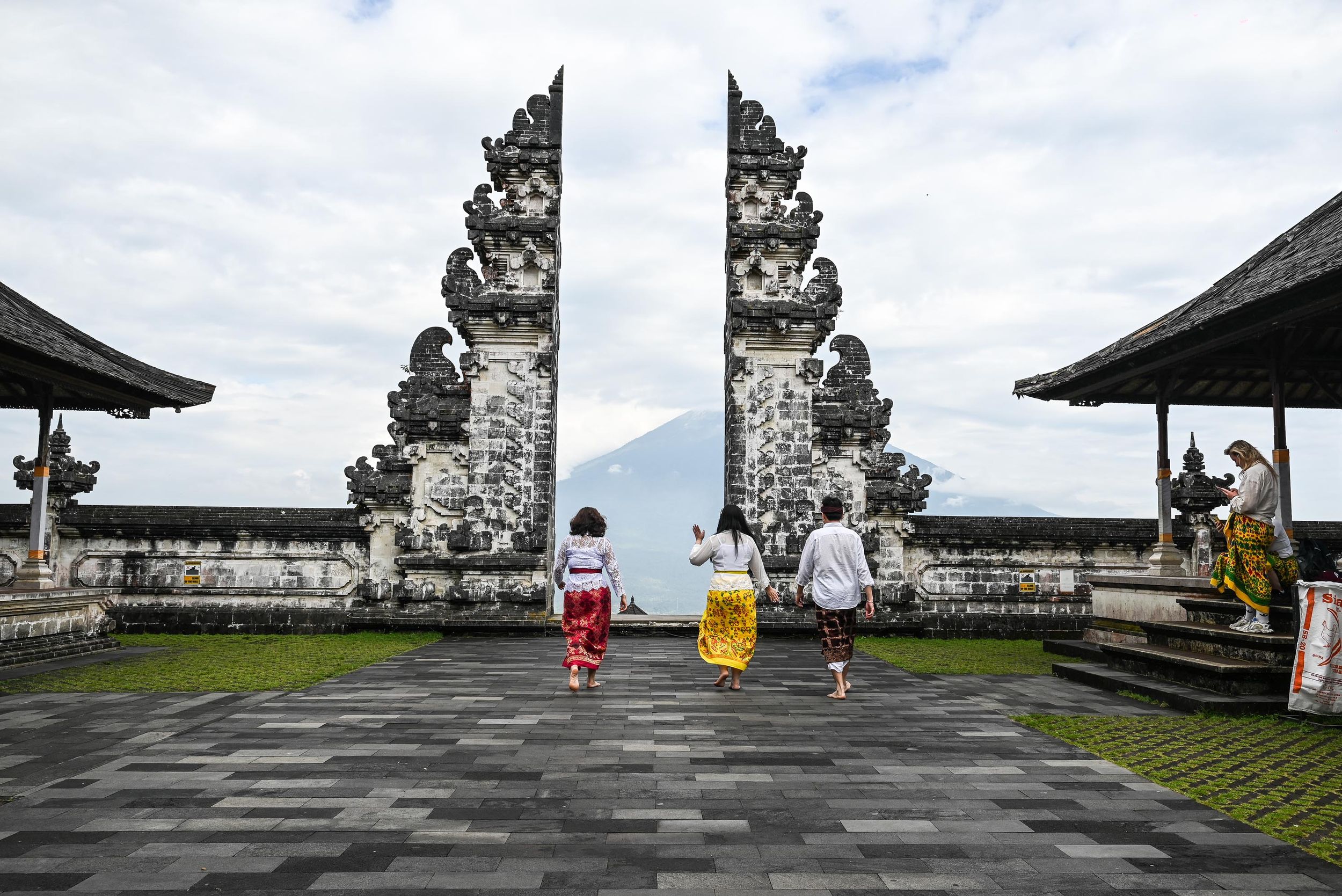 Two tourists walk through the iconic split gate of Pura Lempuyang temple in Bali with Mount Agung in the background.