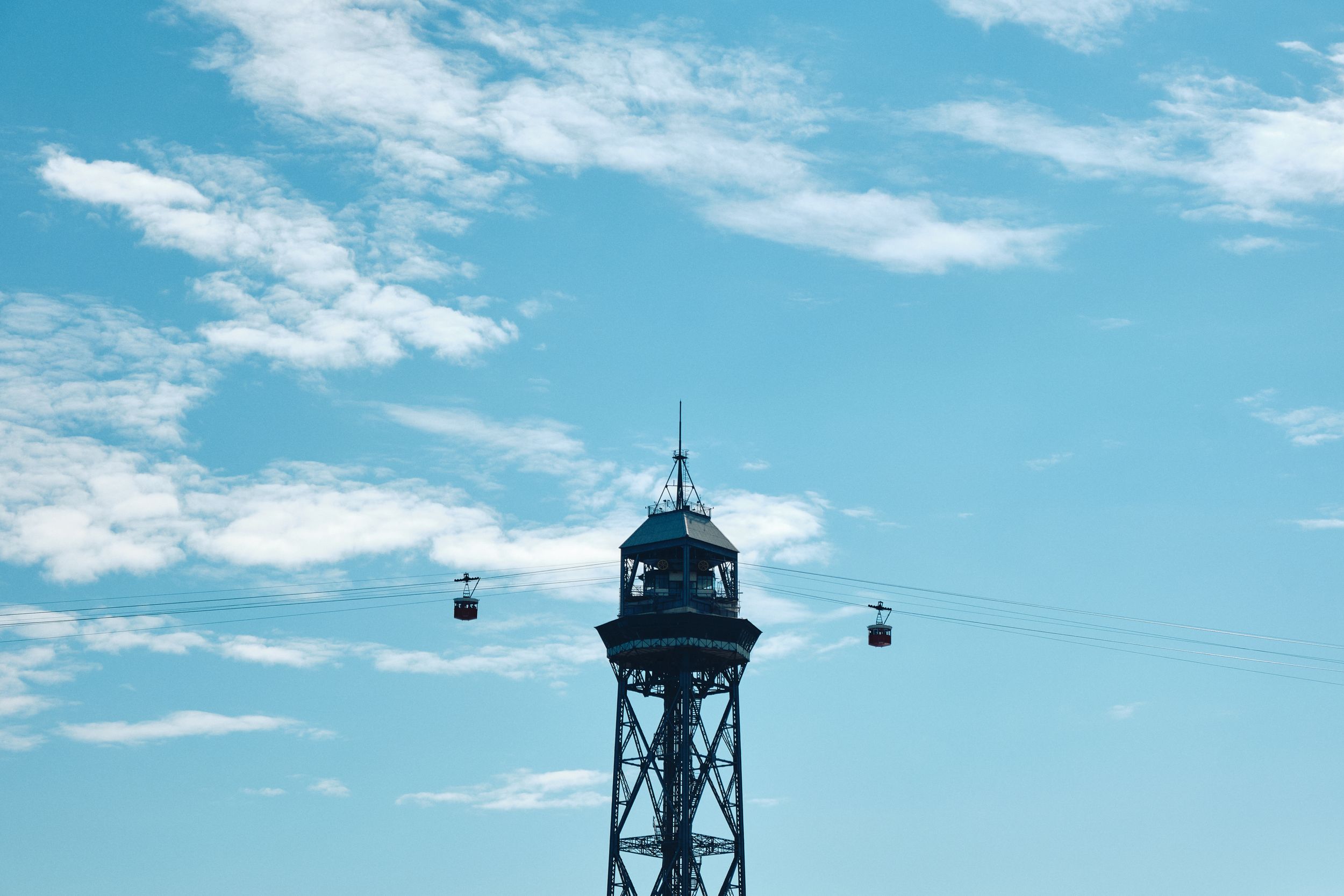 A tall steel cable car tower with two gondolas against a bright blue sky with scattered clouds.