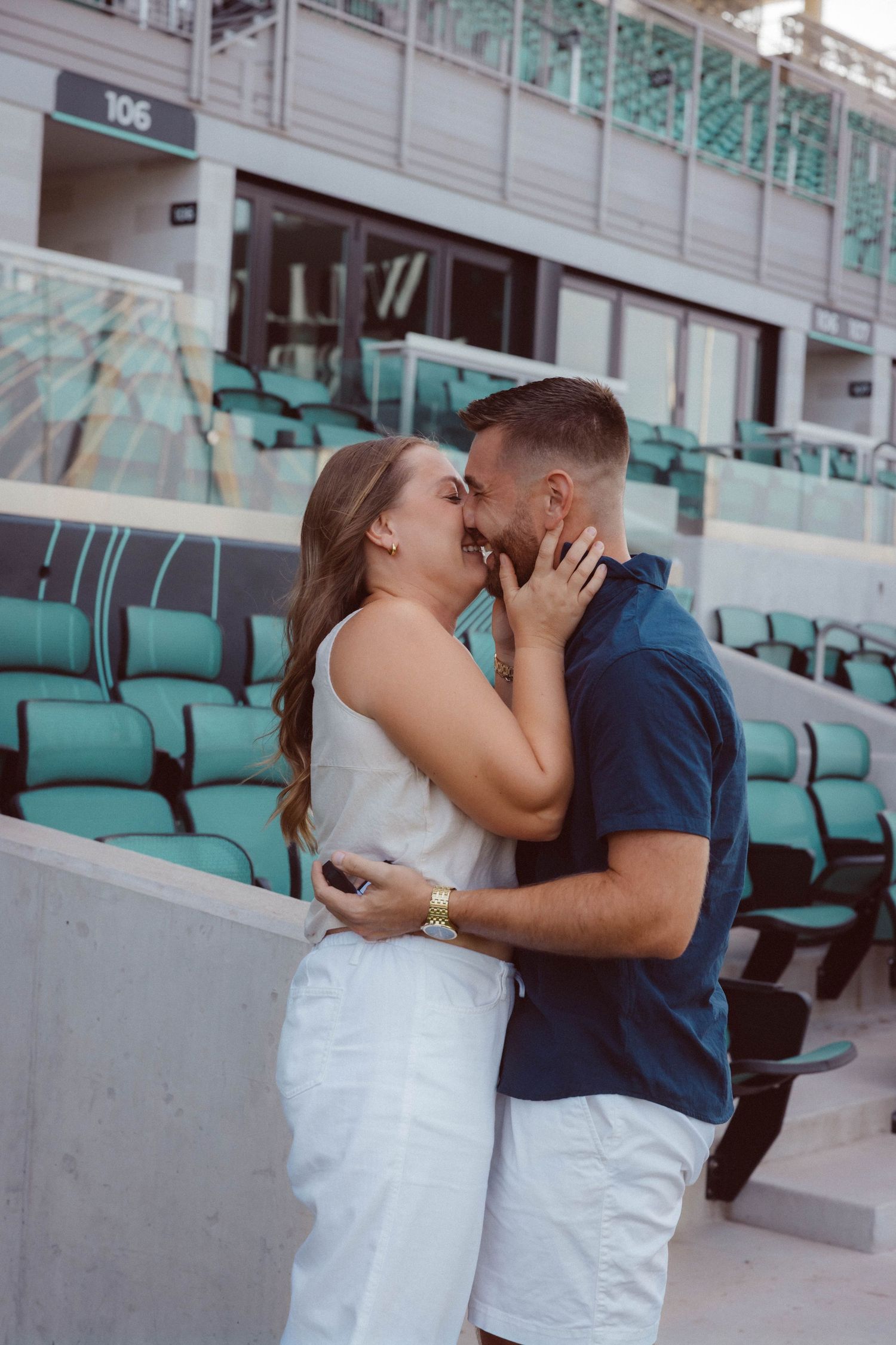 A woman smiles and kisses her new fiancé after saying "yes" to his surprise proposal at CPKC stadium in Kansas City.