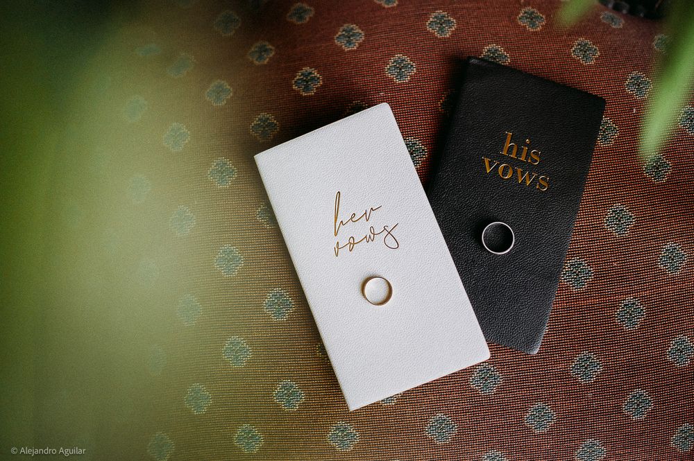 His and her vows booklets with wedding rings on a decorative red and teal patterned background.