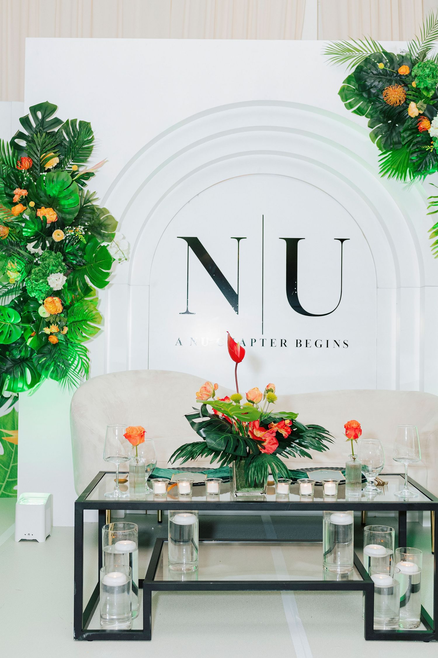 Elegant wedding sweetheart table with tropical floral arrangements, candles, and NU monogram backdrop sign.
