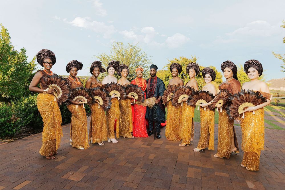 Bridal party in traditional African attire with gold outfits and feathered fans posing outdoors.