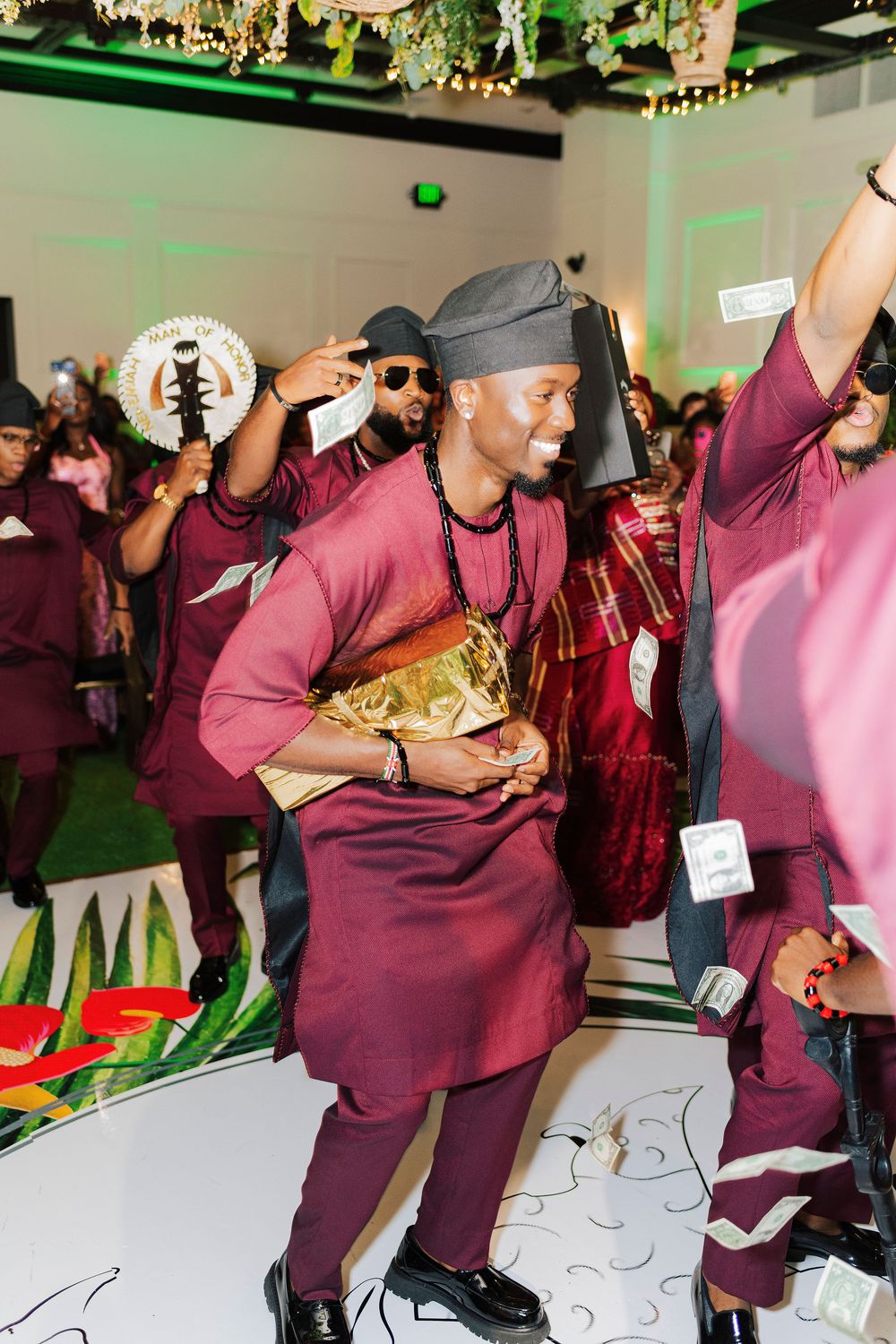 Men in maroon traditional African attire dance joyfully at a vibrant cultural celebration event.