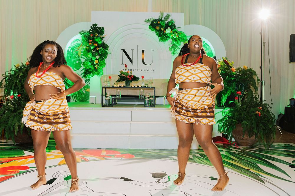 Two women dancing in traditional African print outfits on a white dance floor at an elegant event.