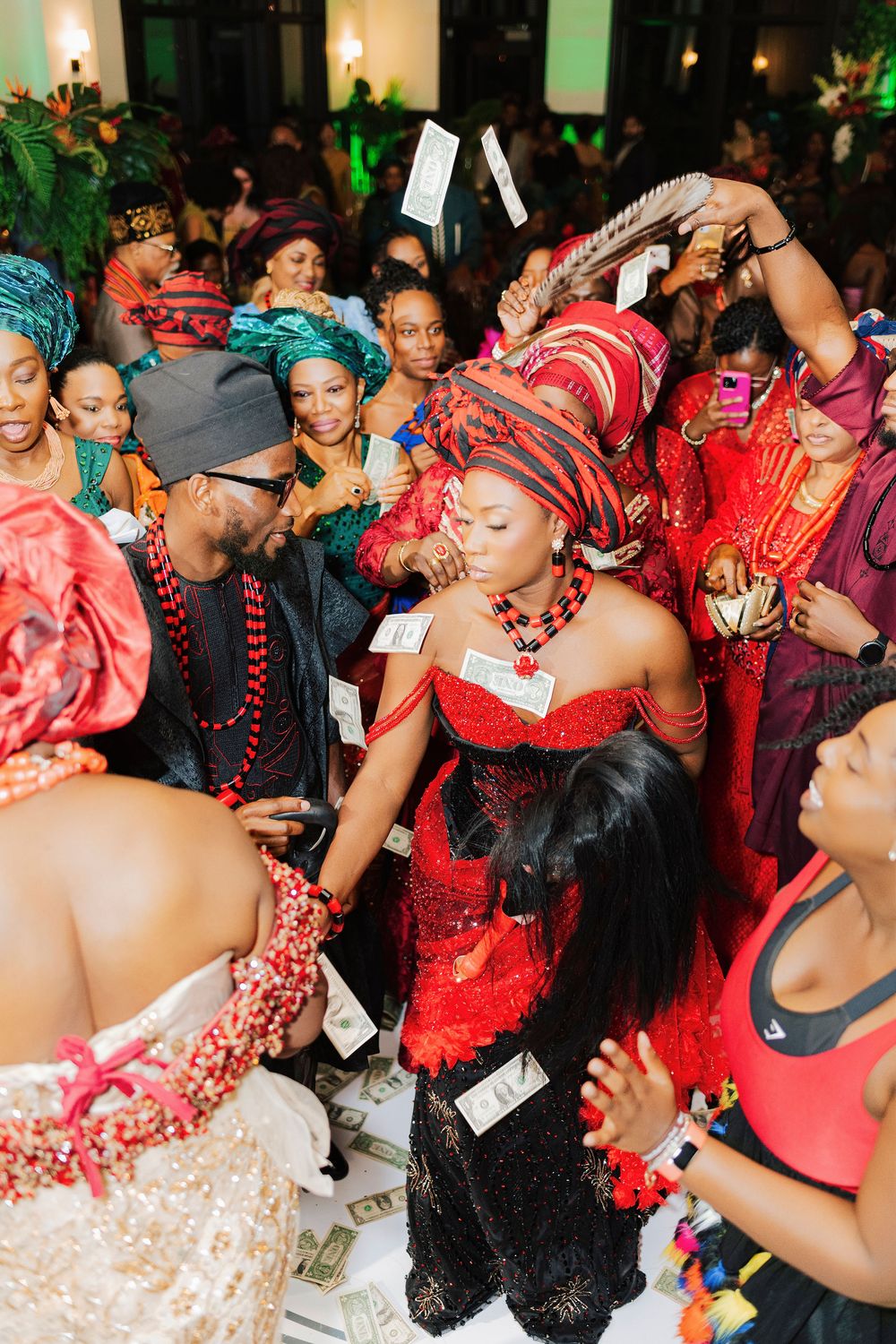 Nigerian traditional wedding ceremony with bride in red attire and groom as guests spray money in celebration.