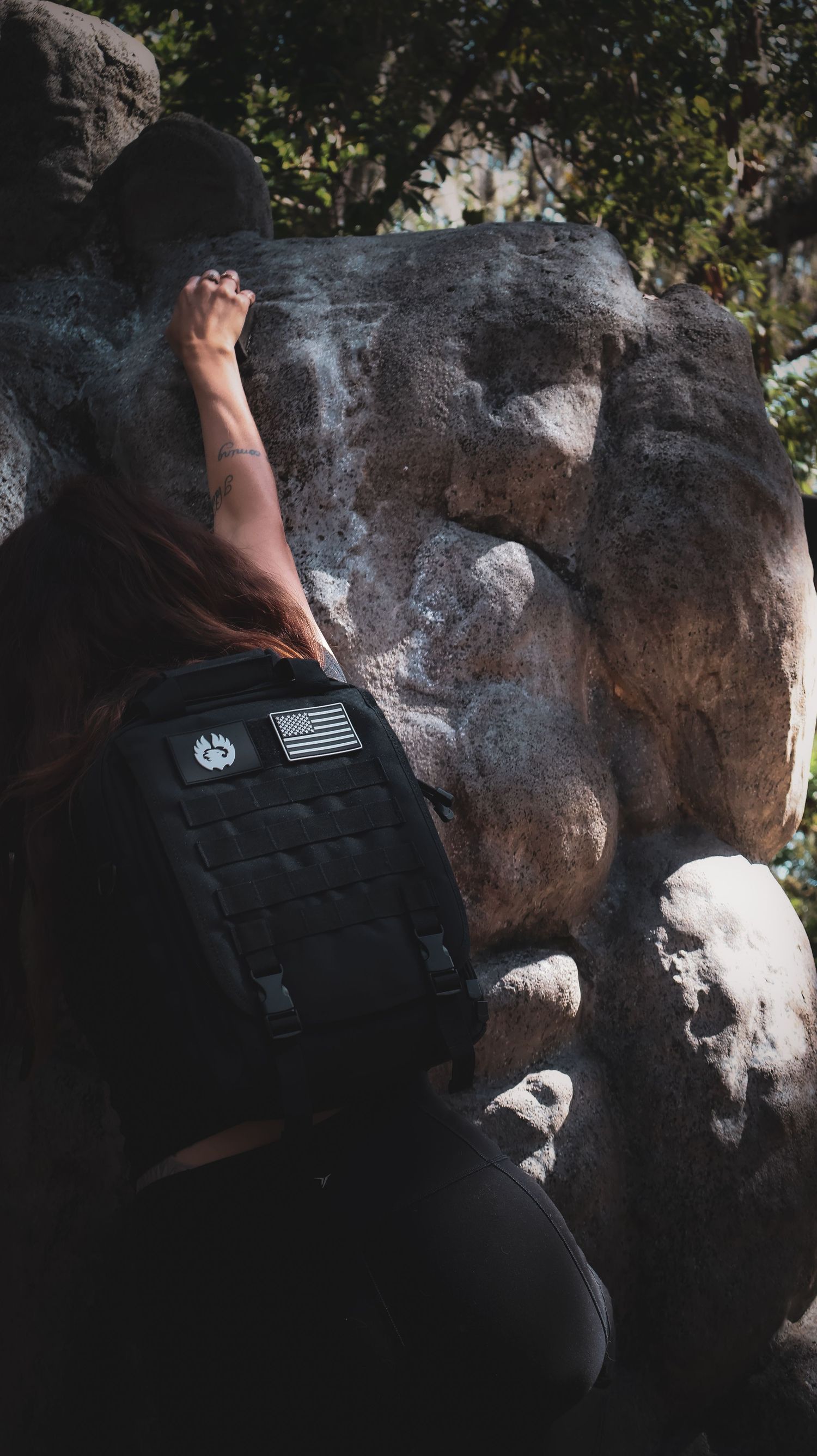 Person with red hair and tactical backpack rock climbing on large boulders outdoors.