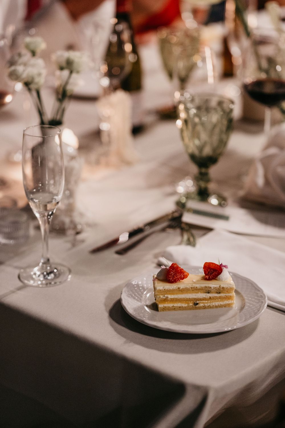 Elegant wedding reception table with a slice of layered cake topped with strawberries on a white plate.