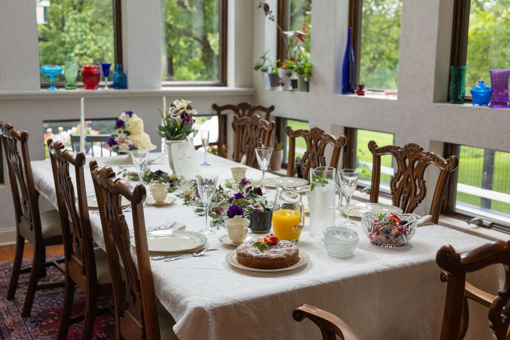Elegant brunch table set for a meal with floral centerpieces, candles, and glassware in a sunlit room.