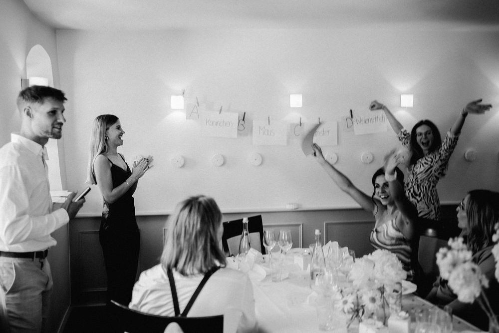 Black and white photo of guests celebrating at a wedding reception dinner party with raised arms and laughter.