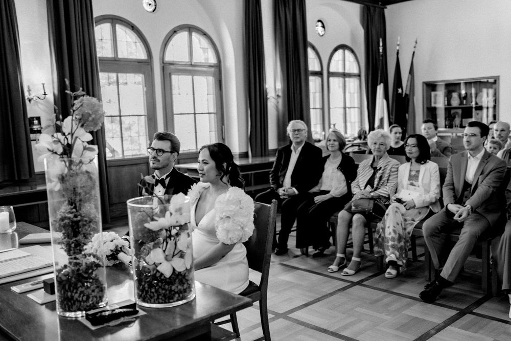 Black and white photo of a wedding ceremony with guests seated in rows inside an elegant hall.