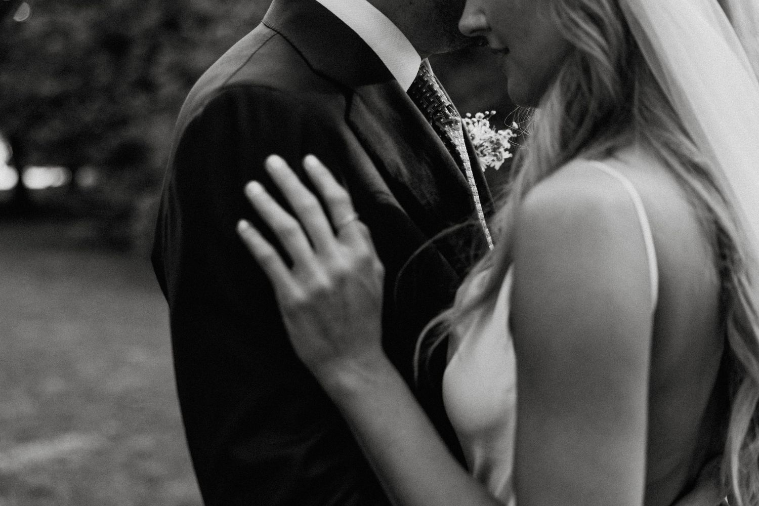 Black and white photo of a wedding couple under an elaborate floral arch at a grand estate.