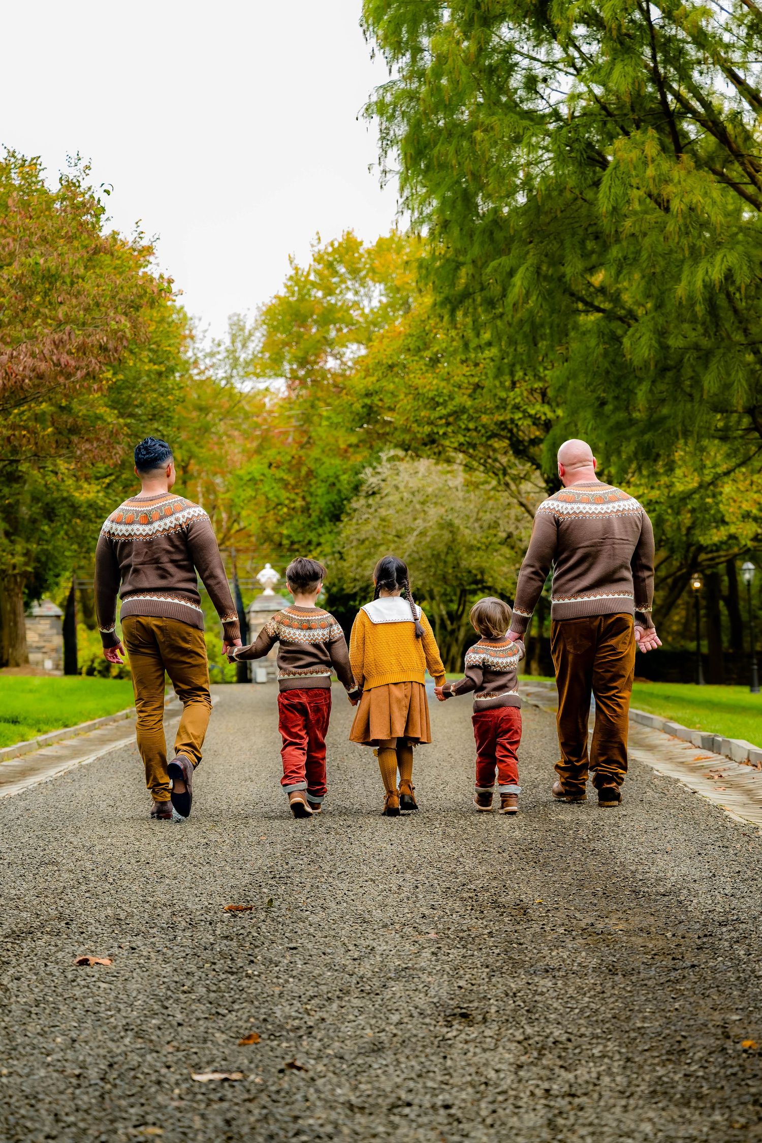 Family of five holding hands walking down a tree-lined path in autumn, viewed from behind.