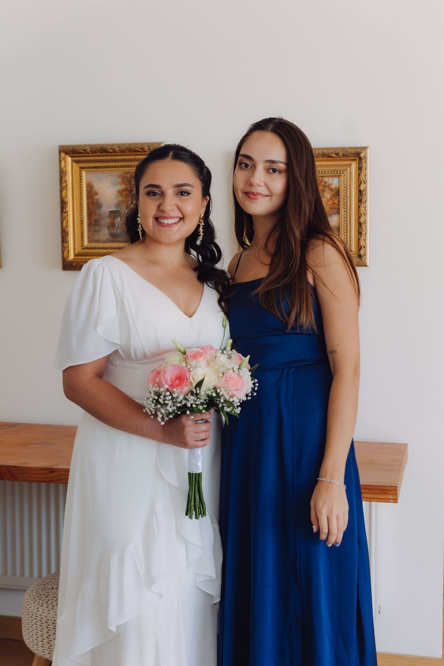 Bride in white wedding dress posing with bridesmaid in royal blue gown holding pink bouquet.