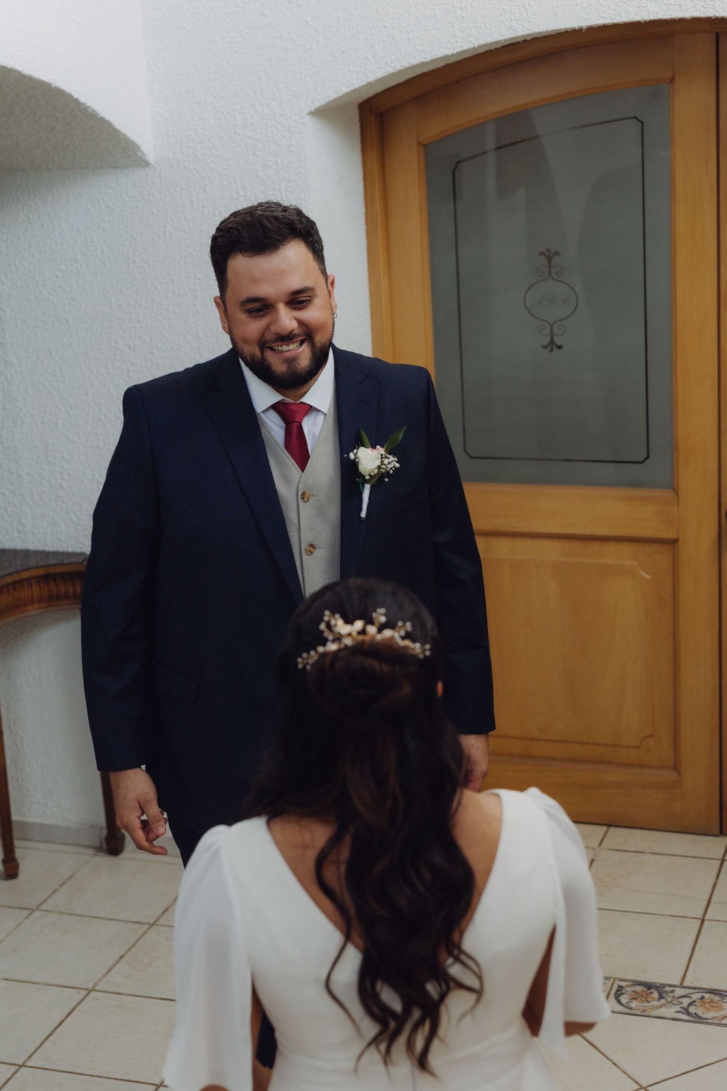 Groom smiles warmly seeing bride in white dress during emotional first look at wedding.