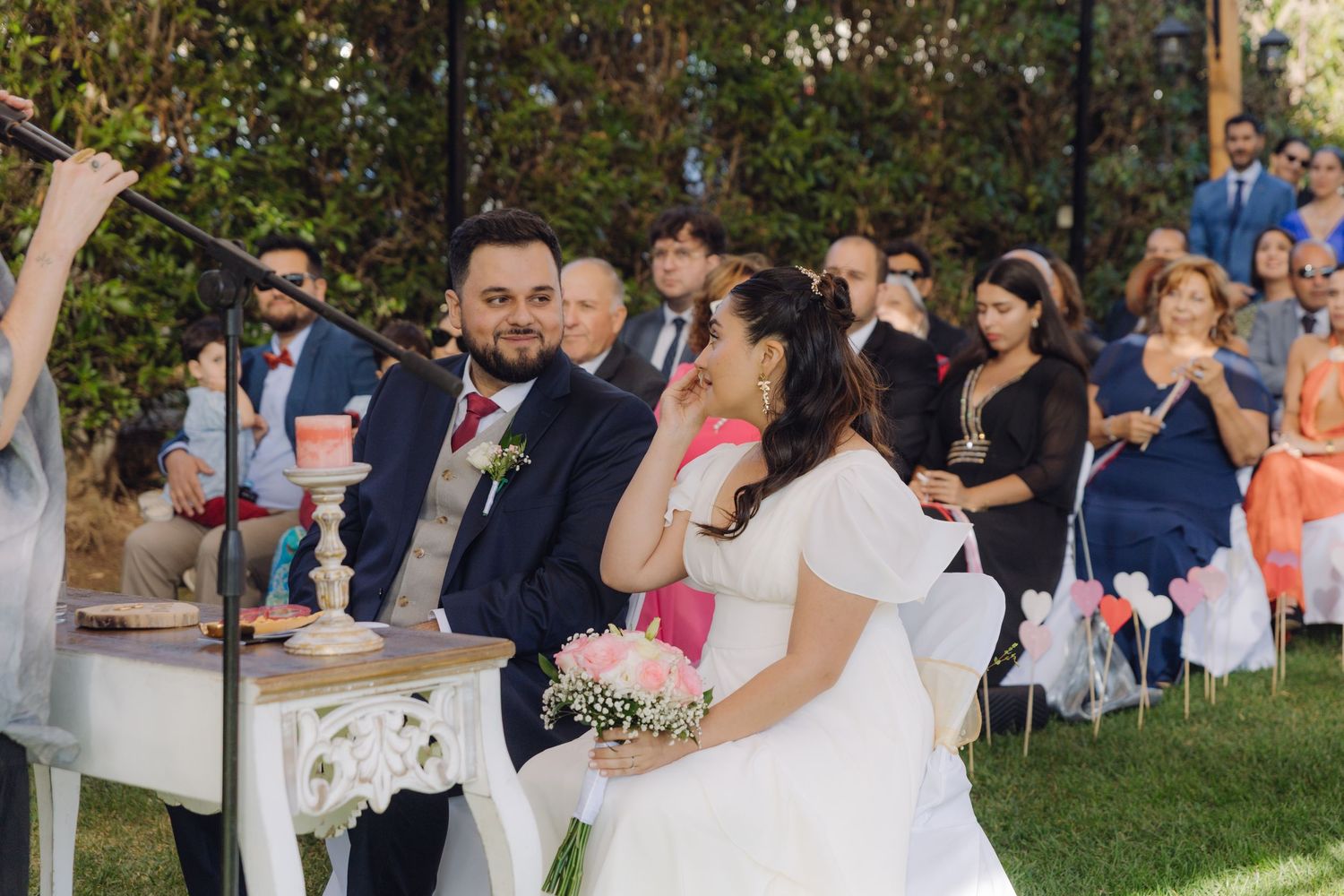 Bride and groom smile during outdoor wedding ceremony with guests seated in rows behind them.