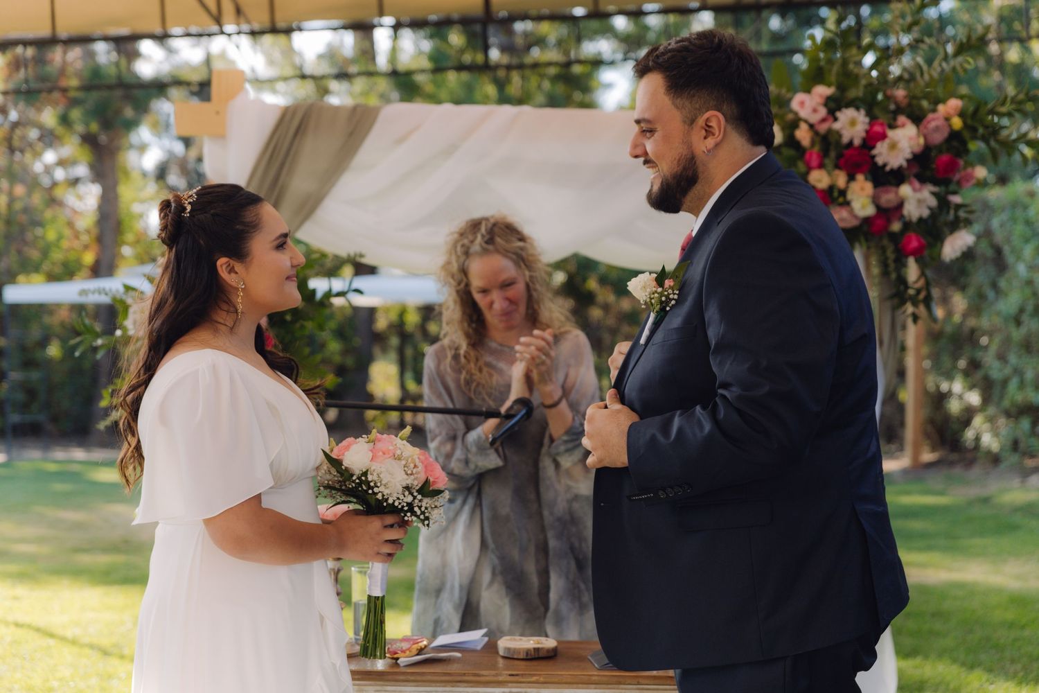 Smiling bride and groom exchange vows before officiant at a beautifully decorated outdoor wedding.