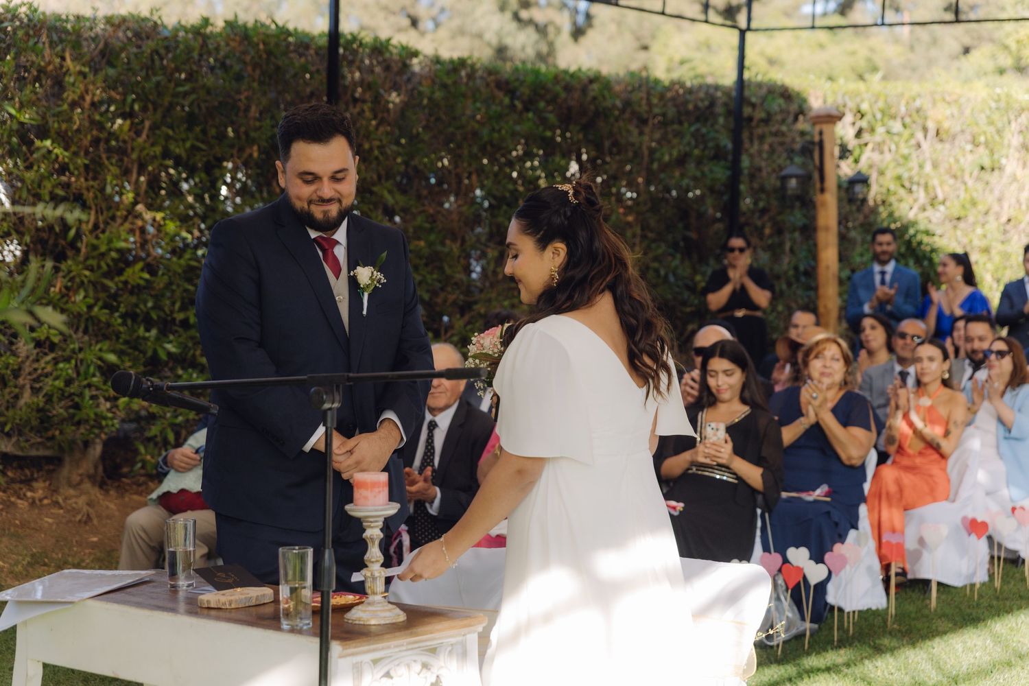 Bride and groom share a moment at outdoor wedding altar while guests applaud in background.