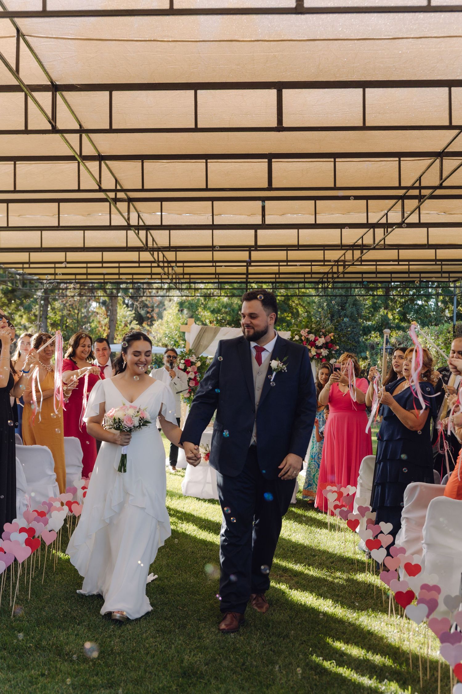 Bride and groom walking down outdoor aisle as guests celebrate with confetti.