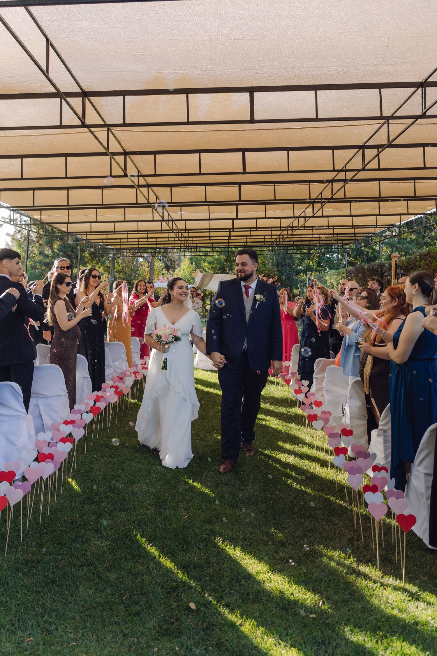 Happy newlyweds walking through confetti-lined aisle during outdoor wedding ceremony.