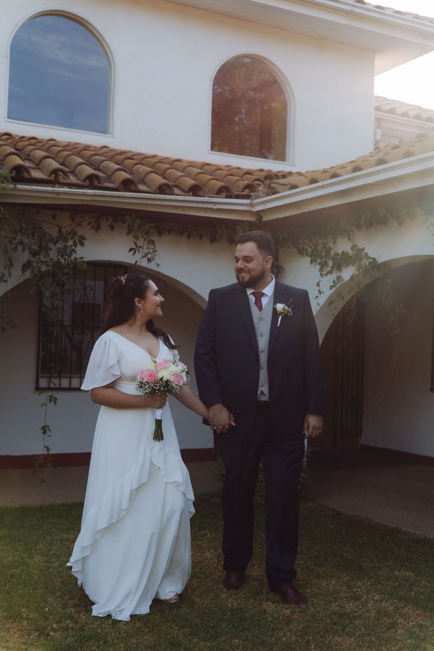 Wedding couple holding hands and looking at each other outside elegant white house.