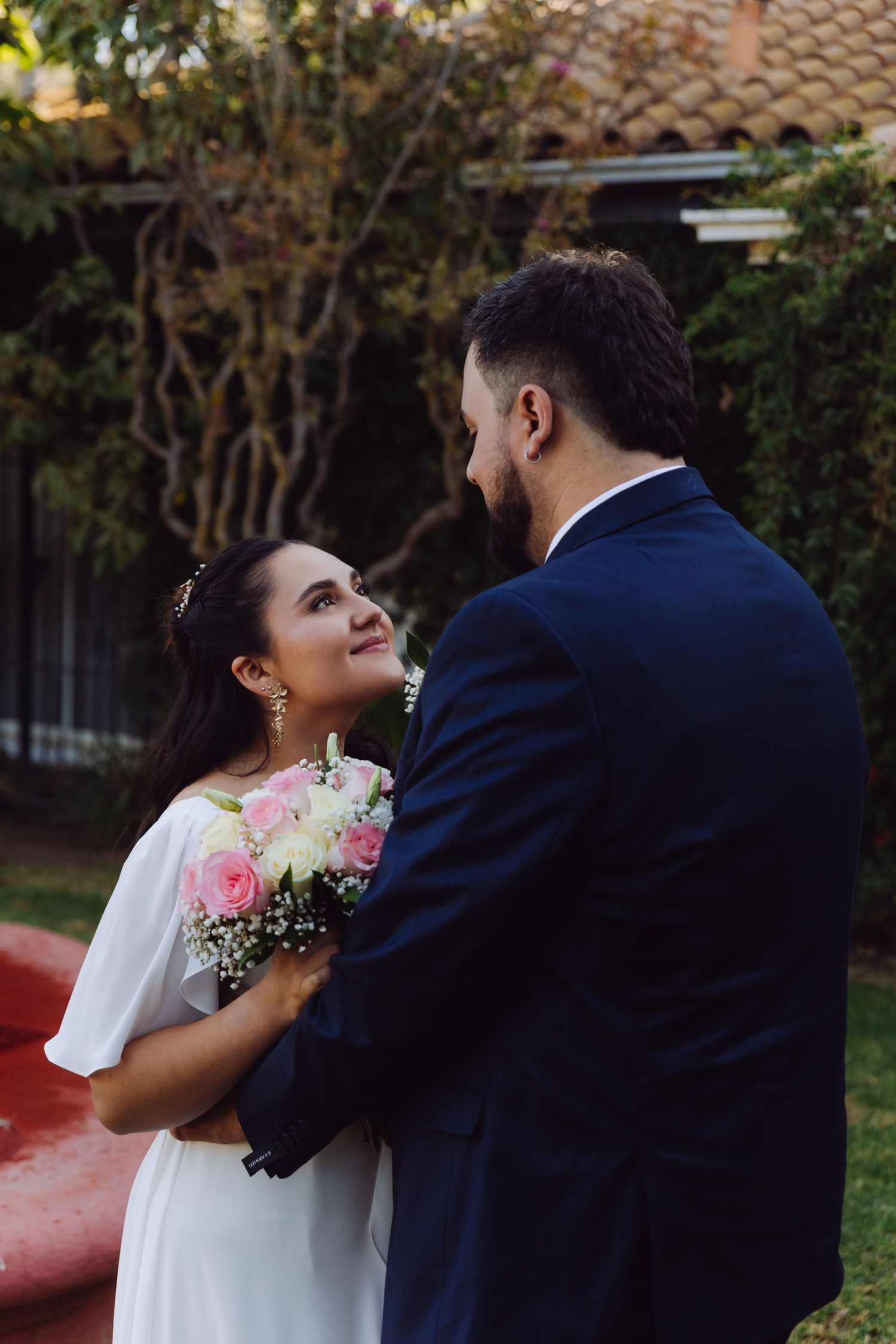 Bride looking up lovingly at groom while holding bouquet in garden setting.
