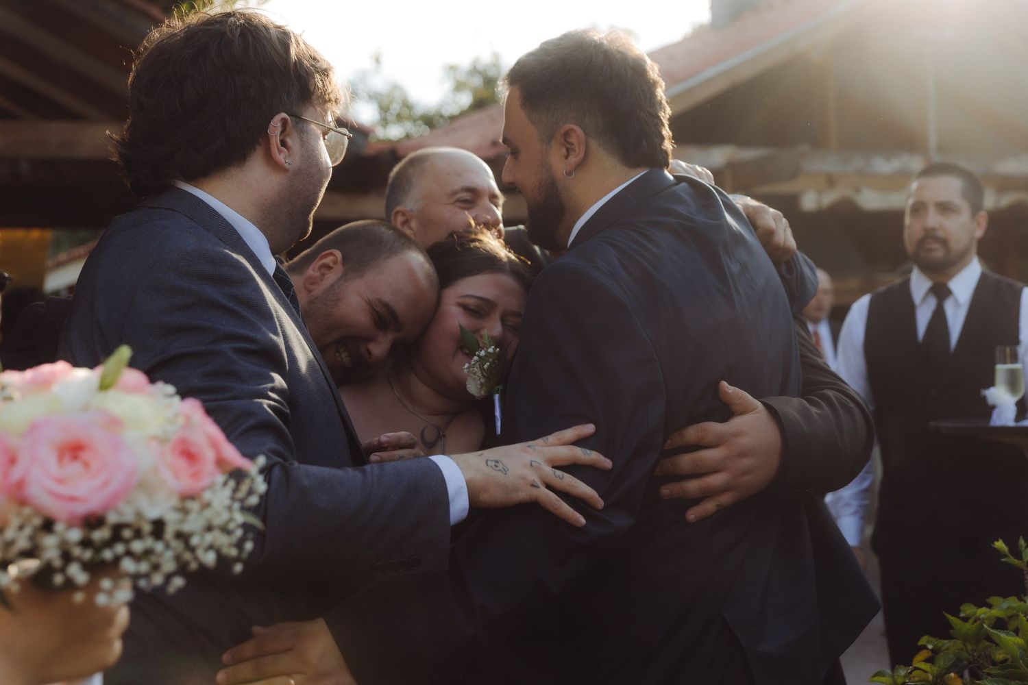 Group of wedding guests sharing a joyful group hug at an outdoor wedding celebration.