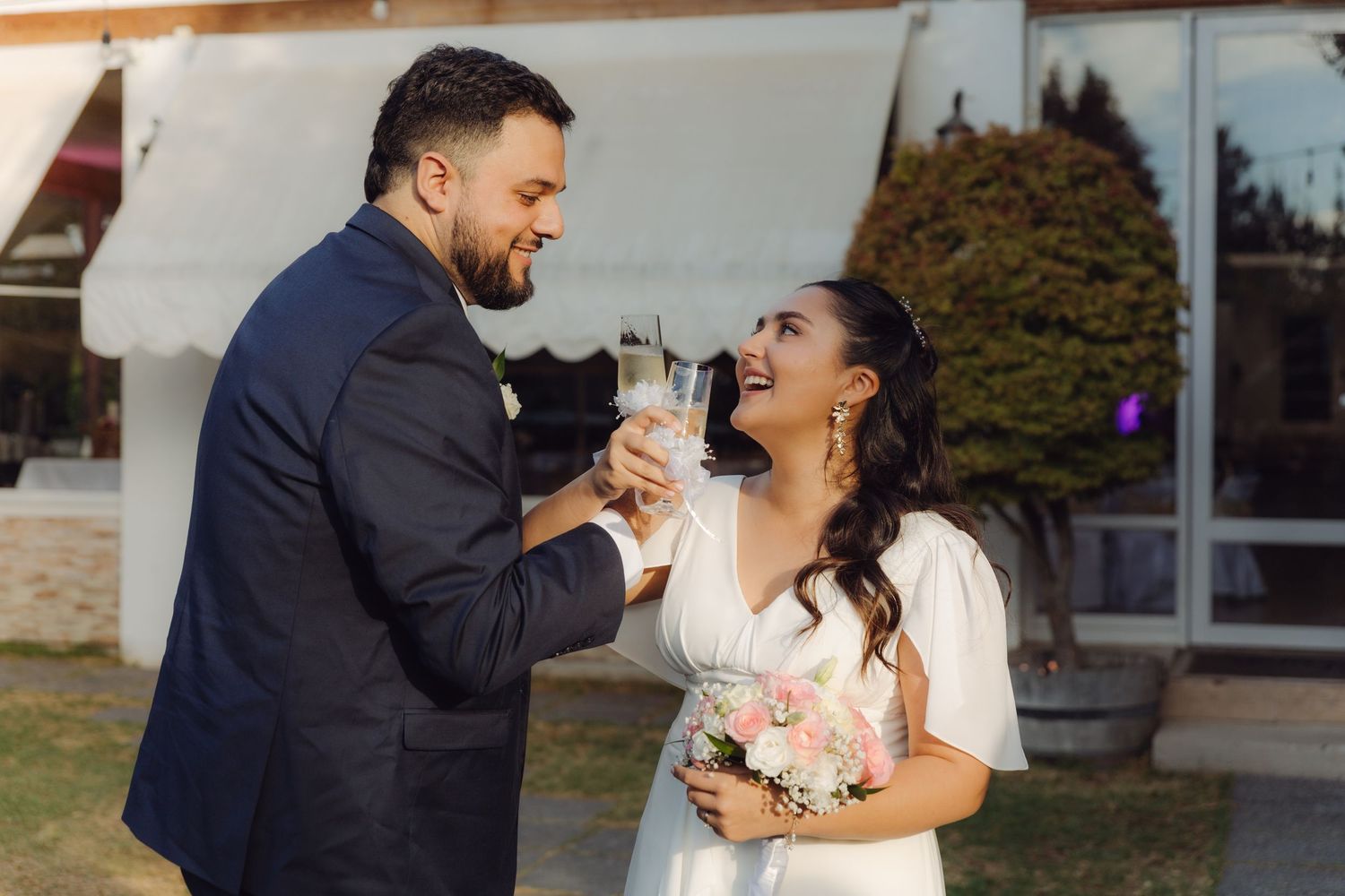 Happy bride and groom laughing while toasting with champagne glasses at their wedding.