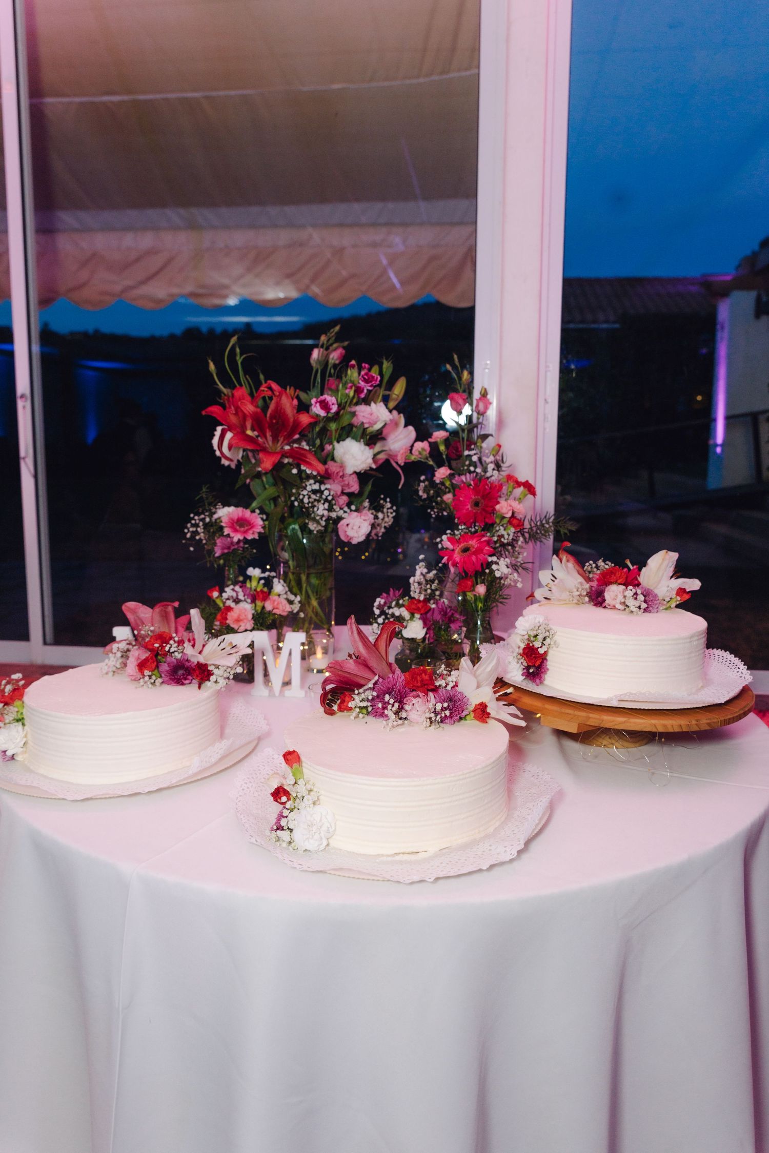 Three white wedding cakes decorated with pink and red flowers on a white tablecloth.