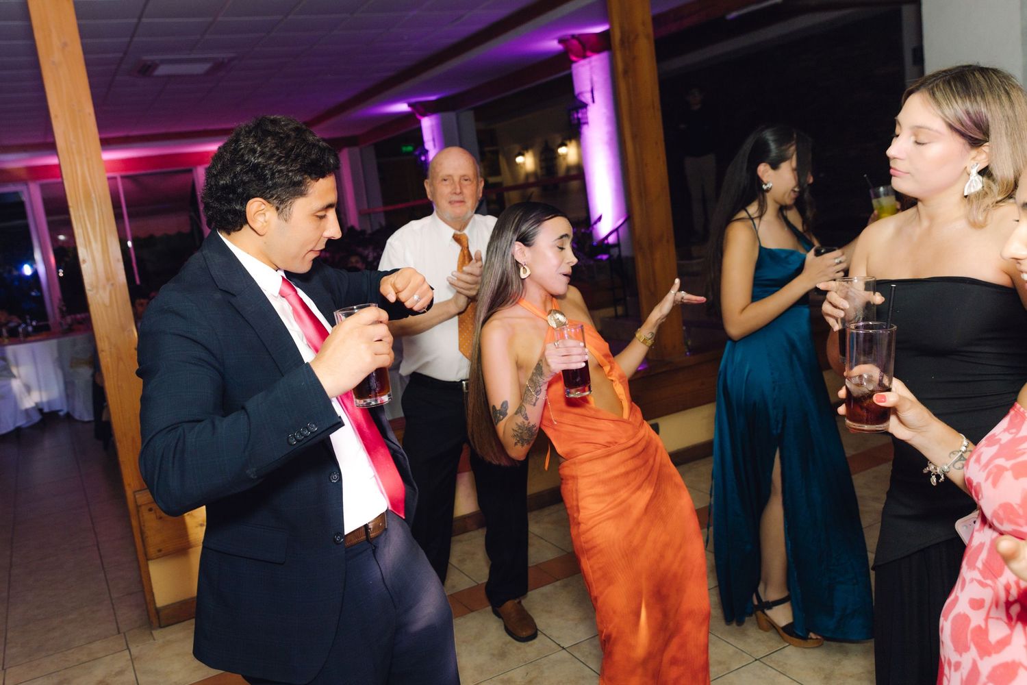Guests dancing and celebrating at a wedding reception in an elegant venue with purple ambient lighting.