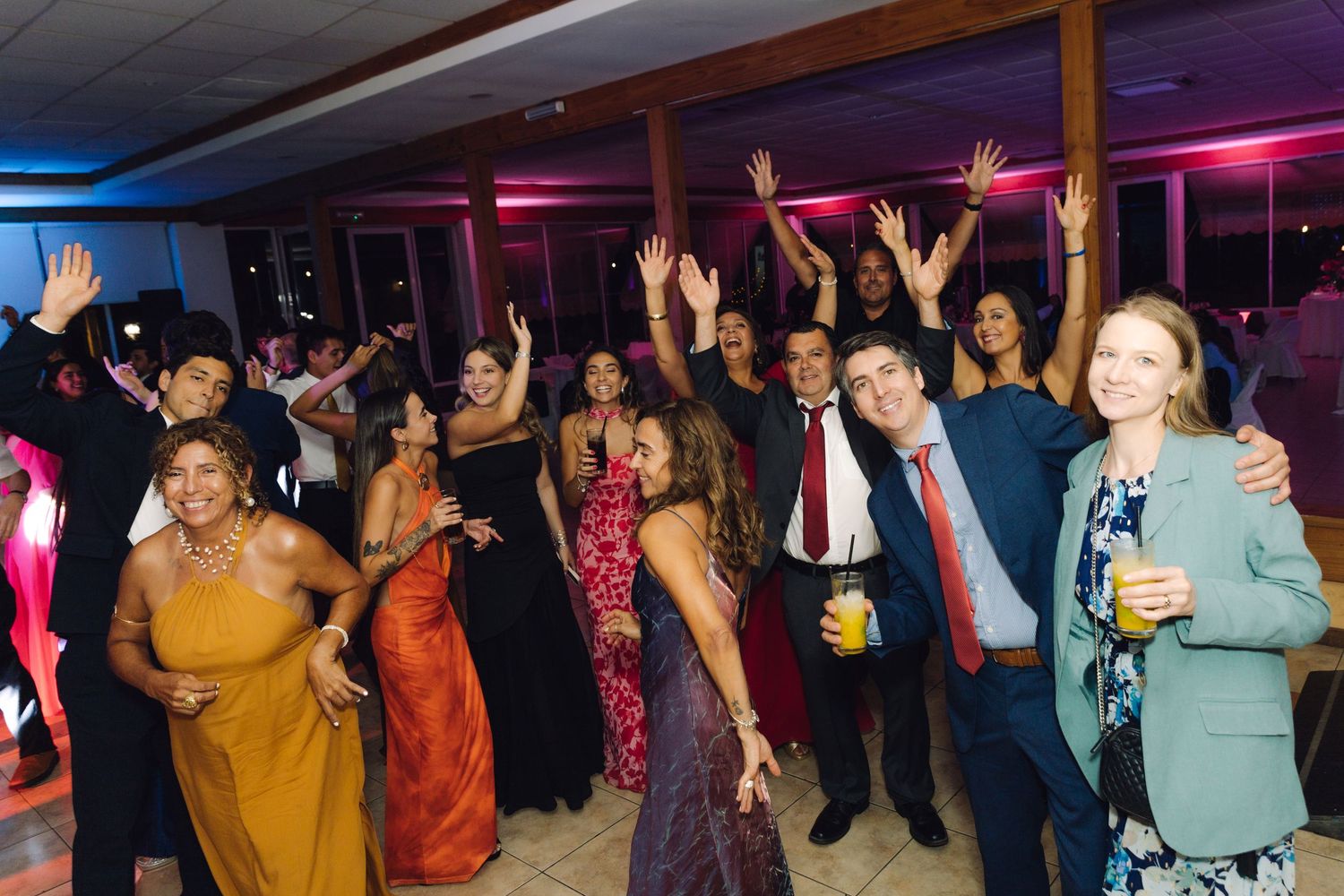 Guests celebrate with hands raised on the dance floor at a festive wedding reception.