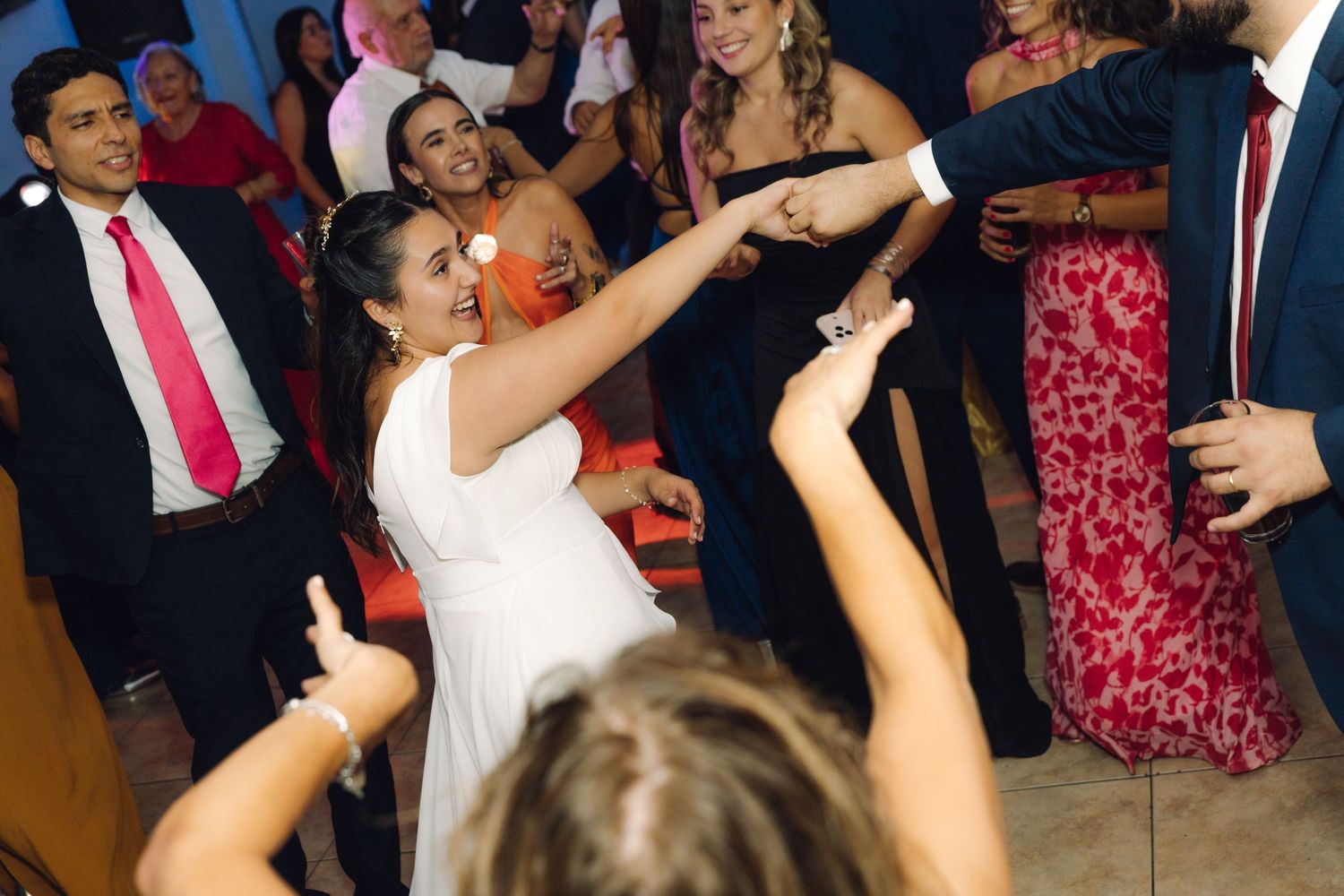 Bride in white dress dances joyfully with guests at a lively wedding reception.