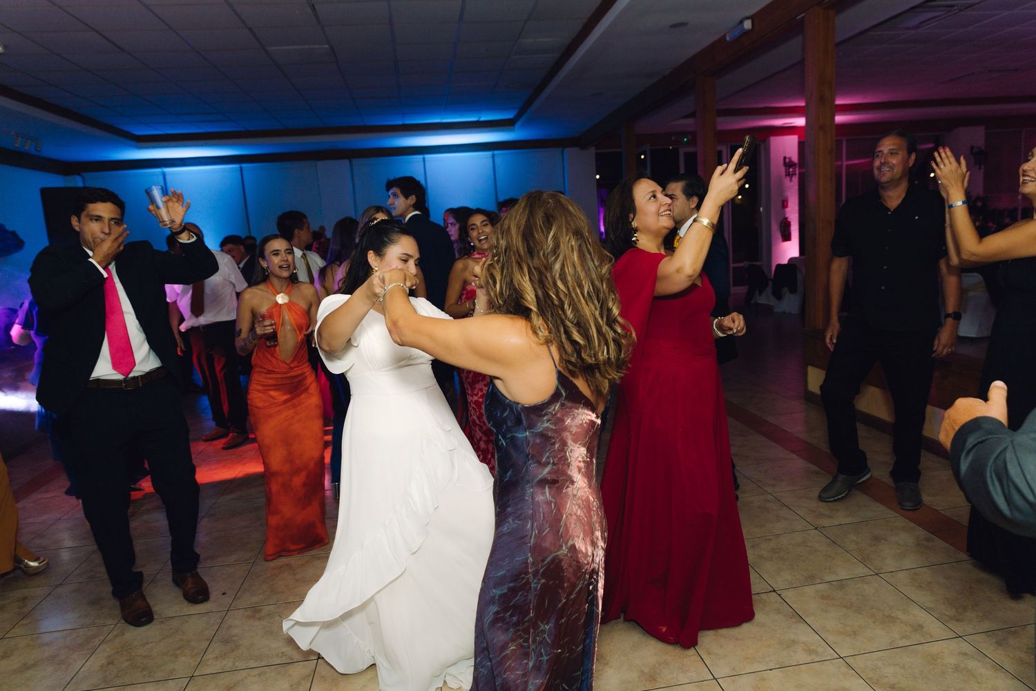 Bride in white gown dances with guests in elegant attire at a wedding reception.