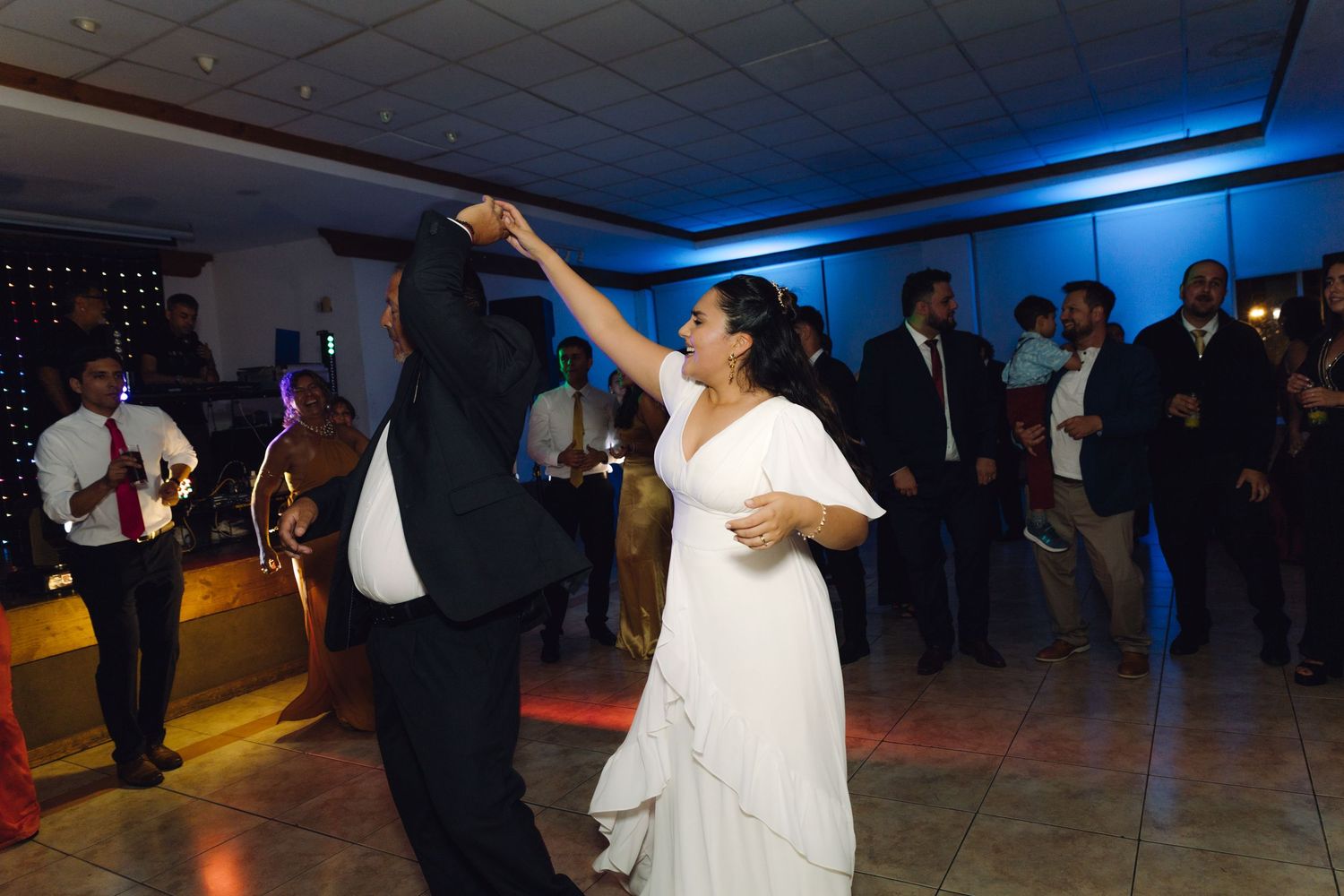 Bride in white dress spins on the dance floor with a guest at wedding reception.
