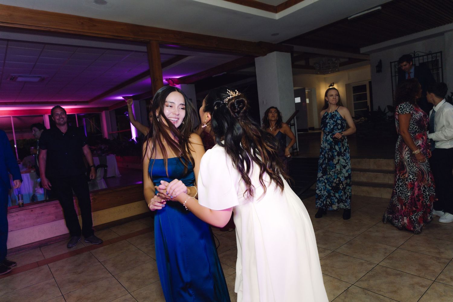 Bride in white dress dances with a guest in blue gown at a wedding reception.