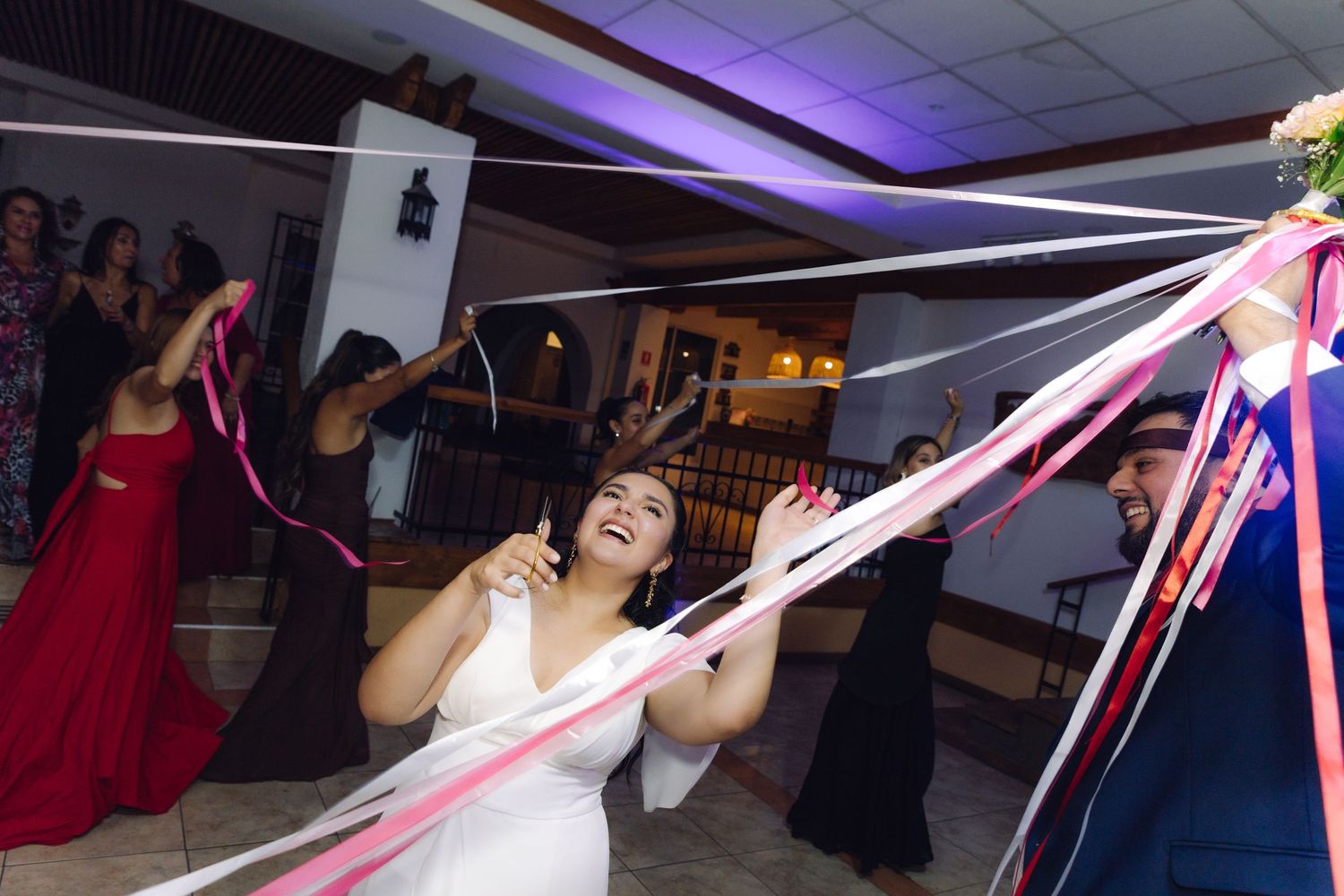 Laughing bride surrounded by colorful streaming ribbons during fun wedding reception activity.