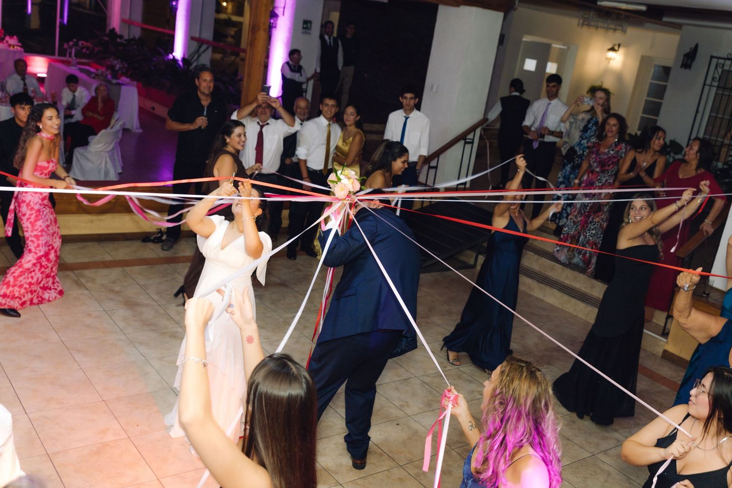 Wedding guests and bride pulling colorful ribbons in a bouquet toss tradition at reception.