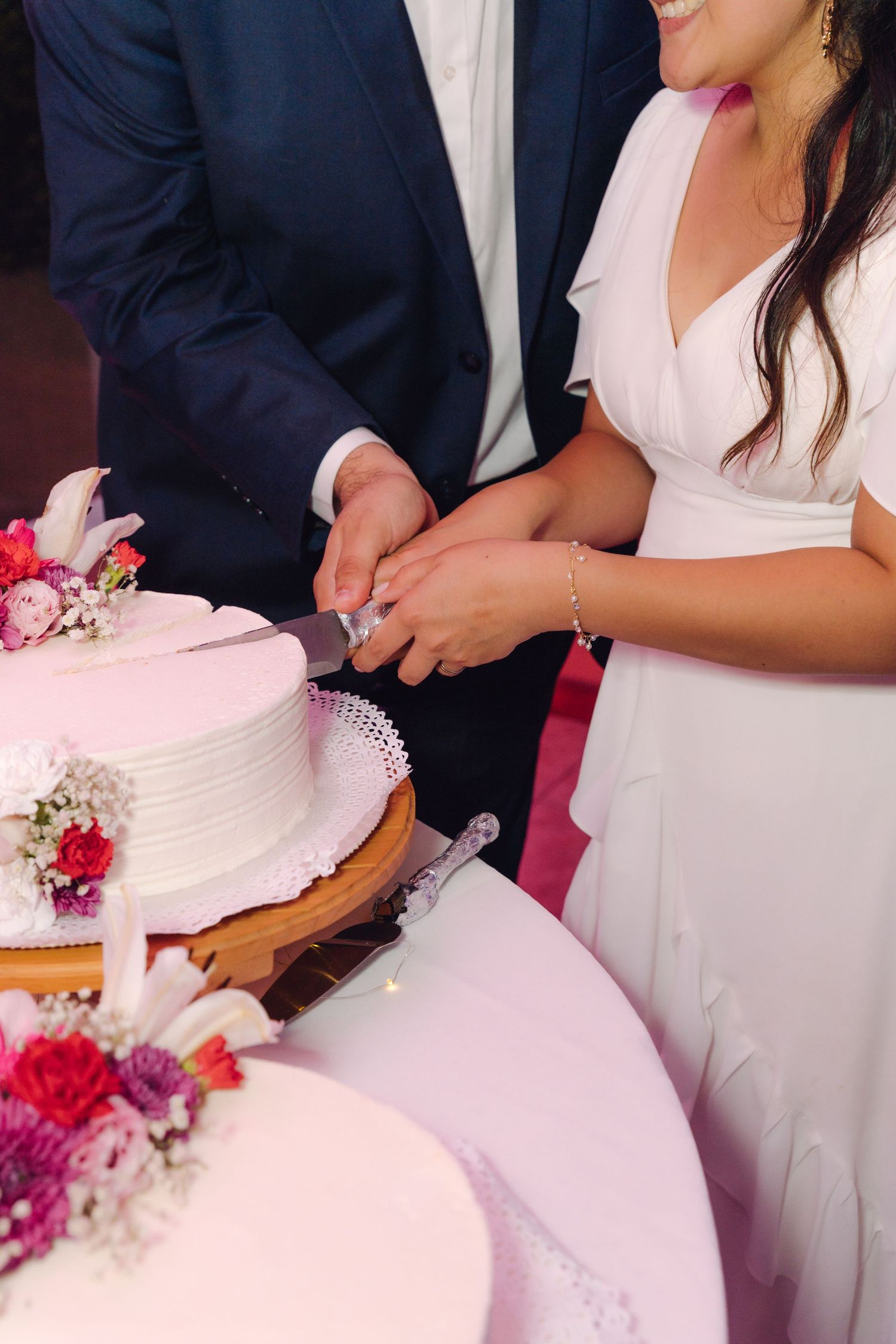 Bride and groom cutting white wedding cake decorated with pink flowers together.