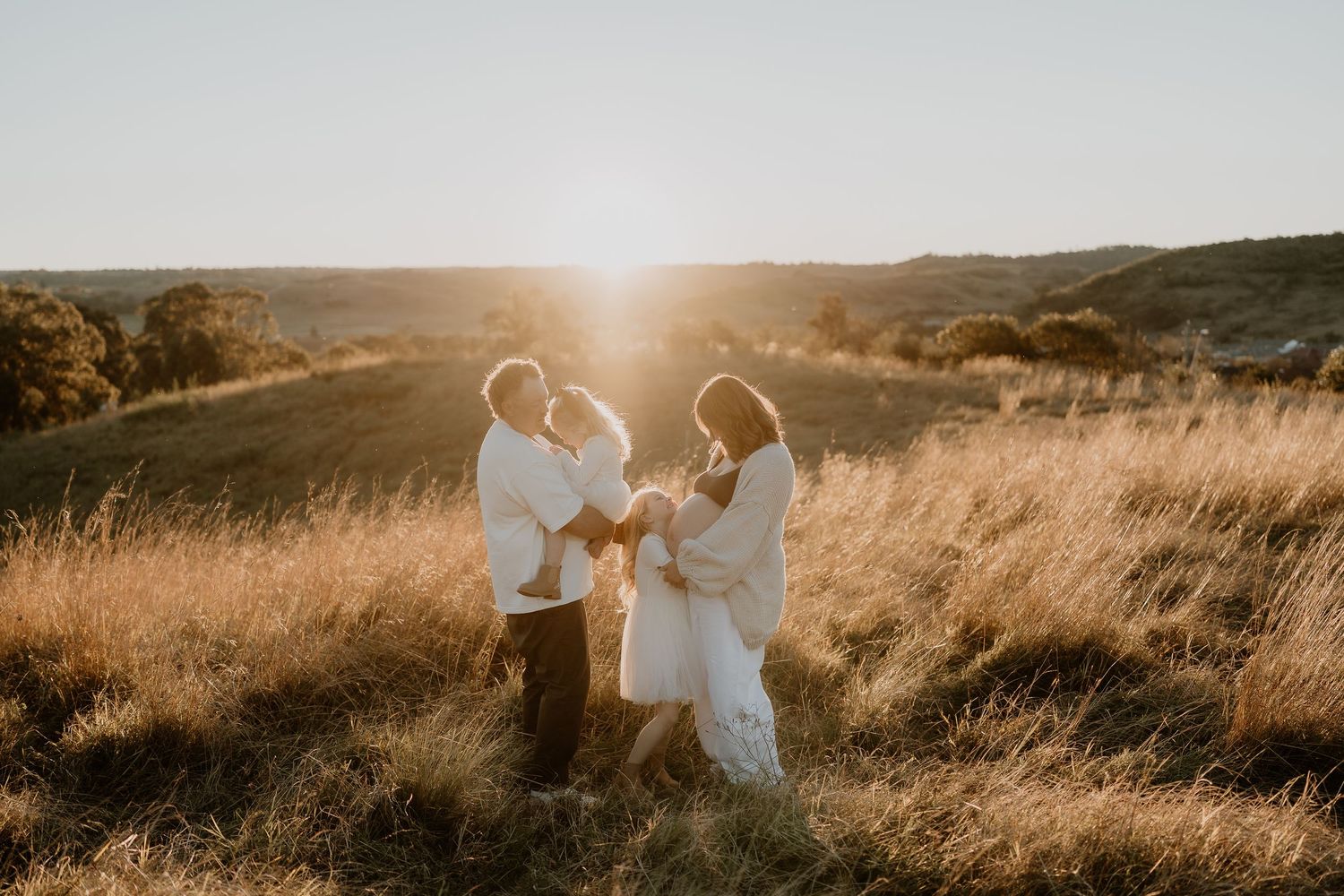 family and pregnant mother in a field at sunset