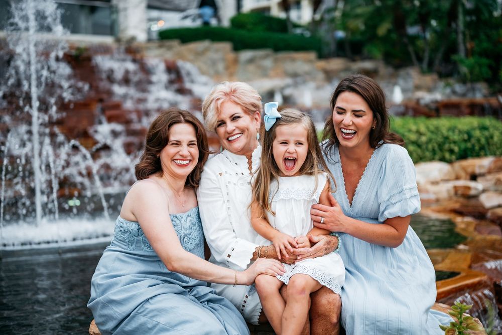 Three women and a cheerful young girl posing and laughing together near a decorative outdoor fountain.