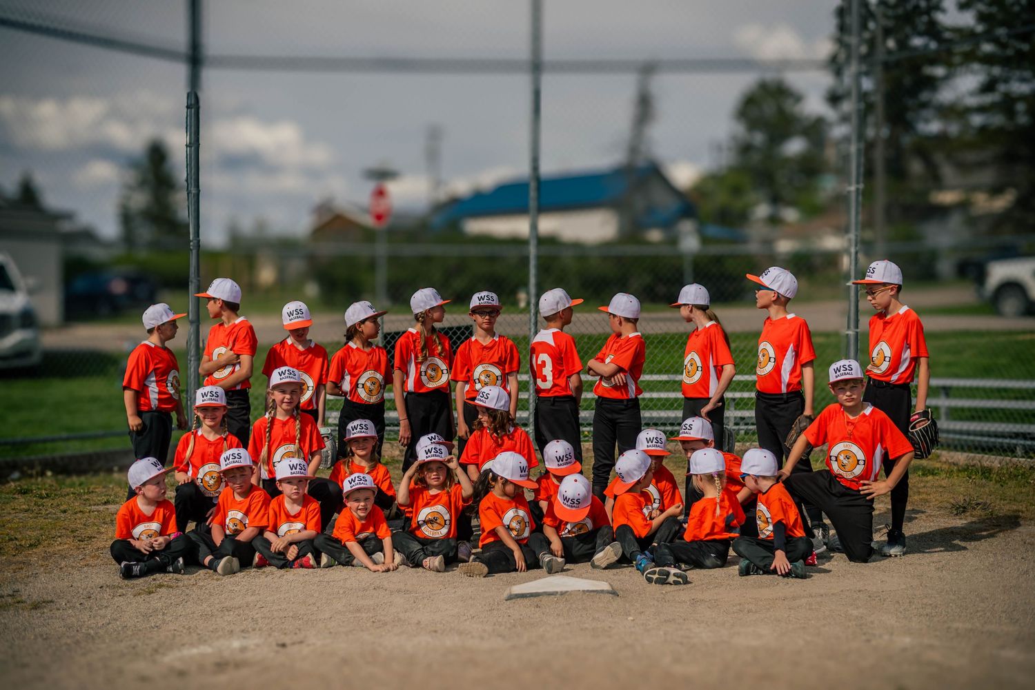 Young baseball team in orange uniforms poses for group photo on baseball diamond outdoors.